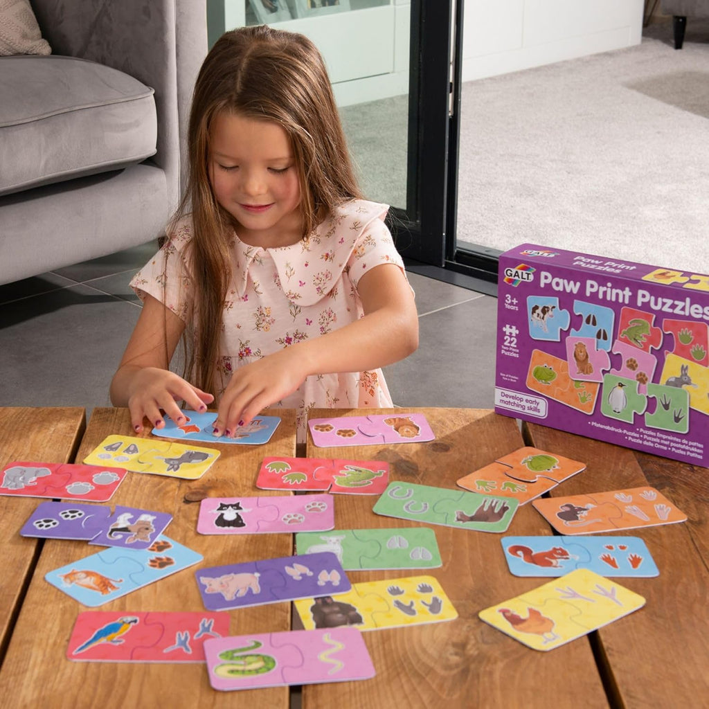 Galt Puzzle - Paw Prints. Young girl playing with paw print puzzles on a wooden table, with the puzzle box in the background.