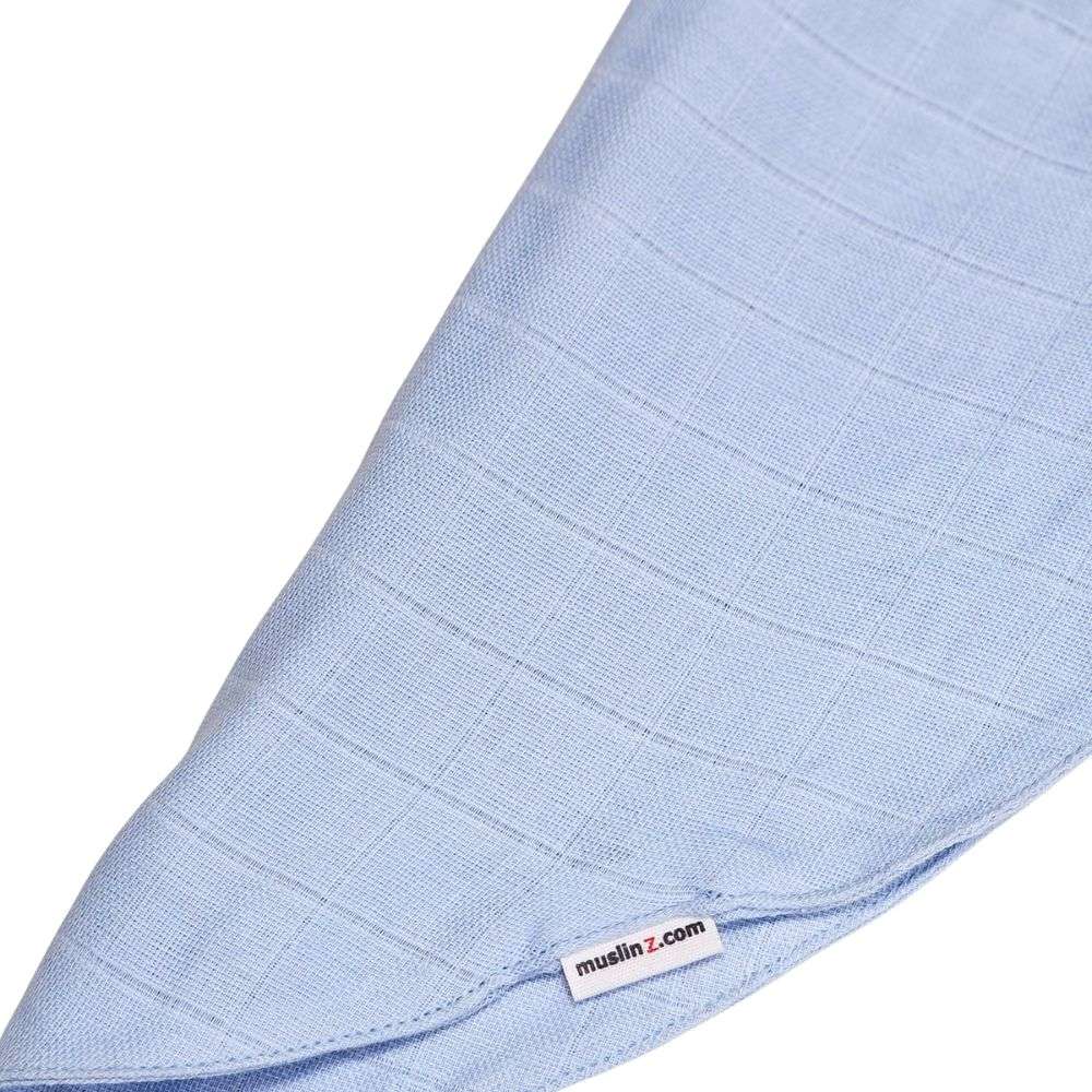 Muslinz Mini Muzi - Pale Blue. Close-up of a light blue muslin fabric with a visible brand label on a white background