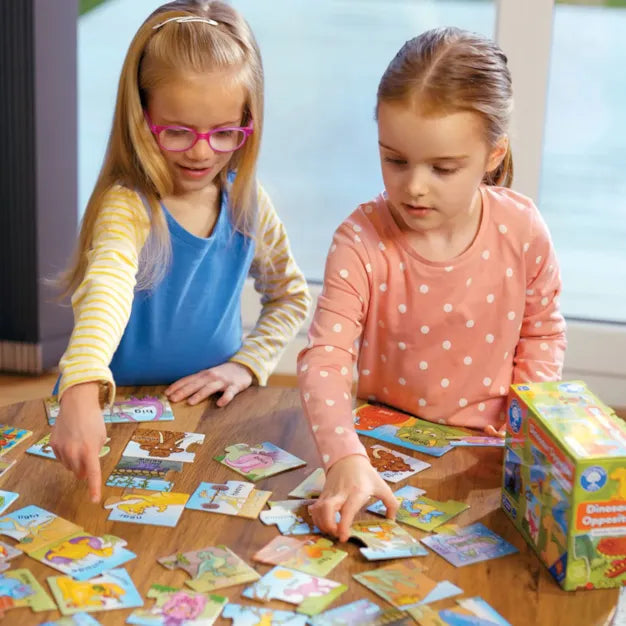 Orchard Toys - Dinosaur Opposites - Two young girls playing with a puzzle on a wooden table.