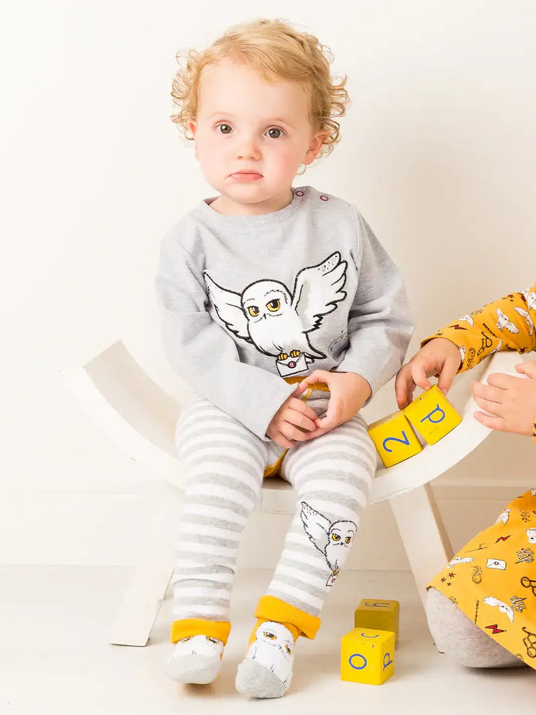 Blade & Rose Harry Potter Hedwig Owl Socks. Child wearing a gray sweater with a owl design and striped pants, sitting on a white chair.