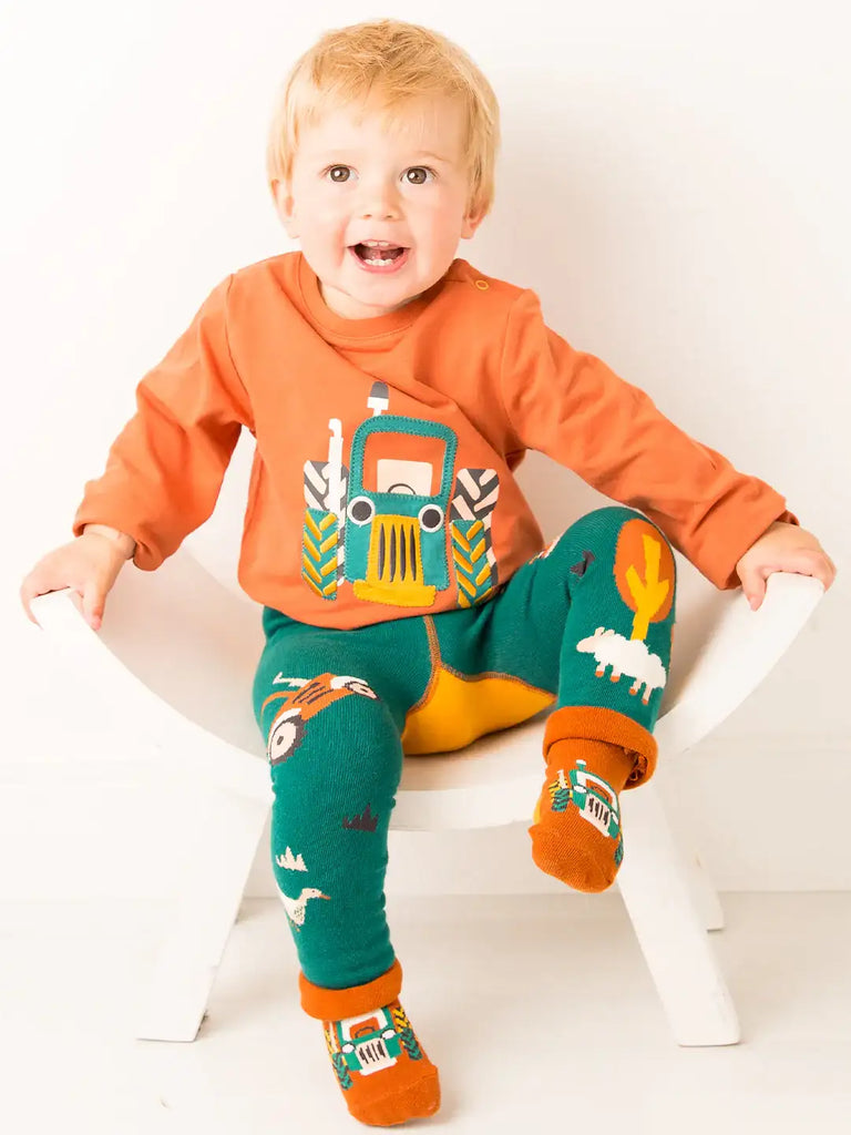 Blade & Rose Rustic Farmyard Leggings. Child wearing an orange shirt with a tractor design, green leggings with animal prints, and orange socks on a white background.