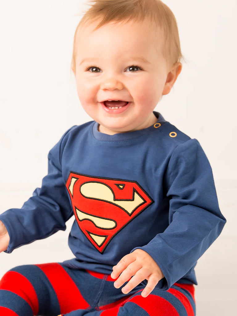 Blade & Rose Superman Top. Baby wearing a blue shirt with a Superman logo and red and blue striped pants on a white background