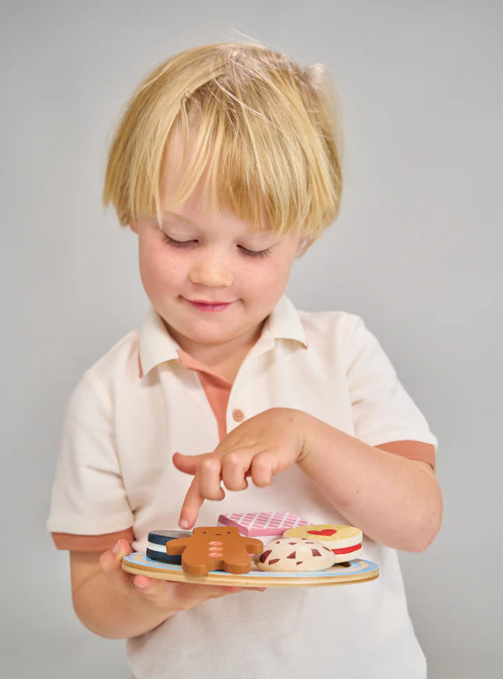 Mentari Tea Time Biscuit Plate. Child holding a wooden toy with biscuit shapes against a gray background