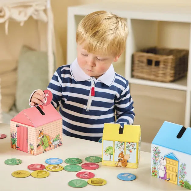 Orchard Toys Peter Rabbit Posting Game. Child playing with colorful house-shaped boxes and number cards on a table.