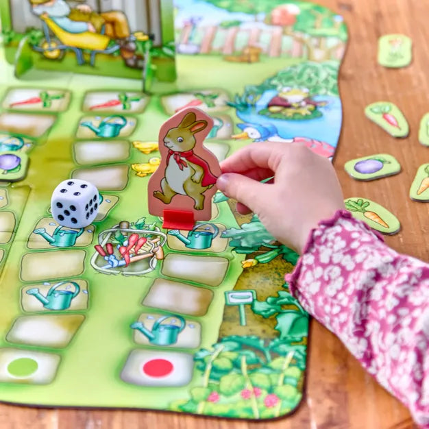 Orchard Toys Peter Rabbit Don't Wake Mr. McGregor Game. Child playing a garden-themed board game with colorful tiles and a dice.