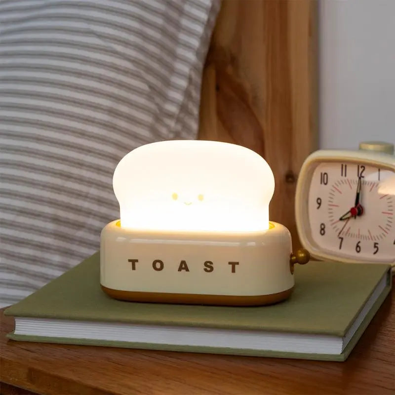 Rex London USB Rechargeable Dimmable Night Light - Kawaii Toaster. Light-up 'TOAST' night light on a book with an alarm clock in the background