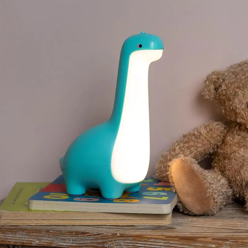 Rex London USB Rechargeable Dimmable Night Light - Dinosaur. Dinosaur-shaped night light on a stack of books with a teddy bear in the background