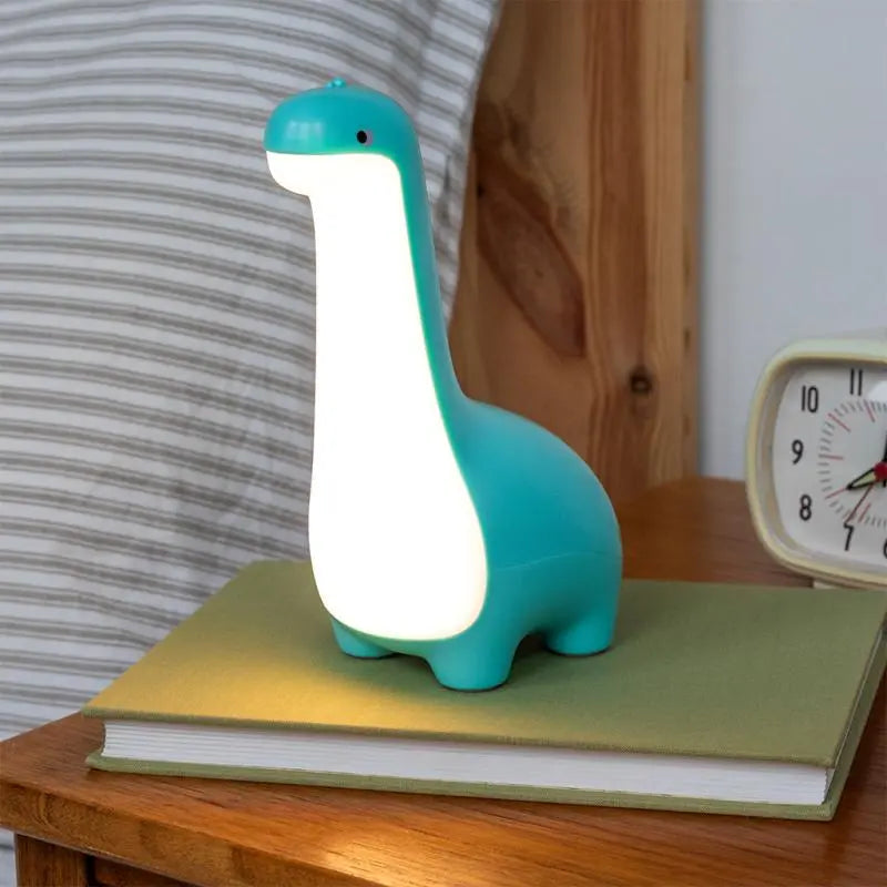 Rex London USB Rechargeable Dimmable Night Light - Dinosaur. Dinosaur-shaped night light on a book with a clock in the background