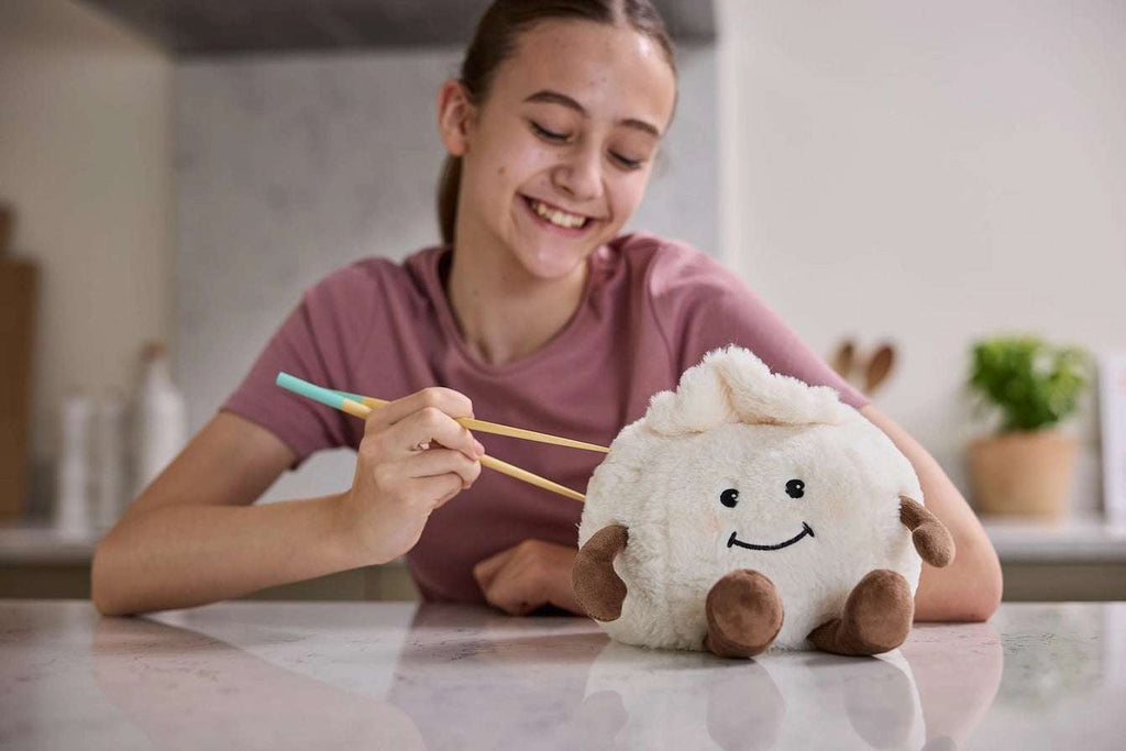 Warmies Dumpling - Person holding chopsticks with a plush toy dumpling on a kitchen counter