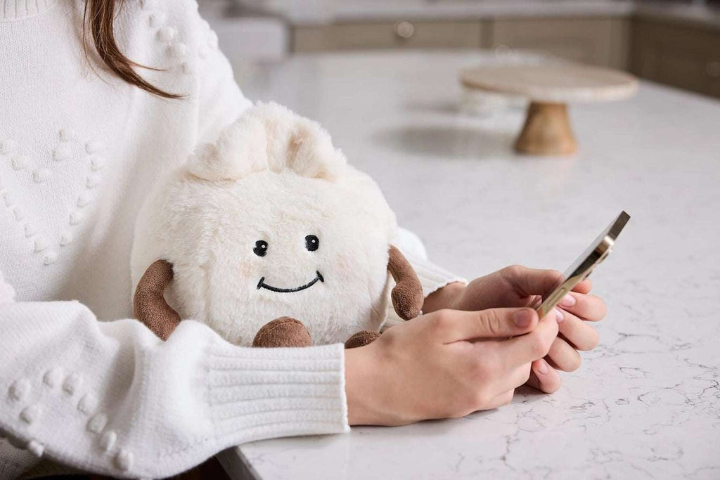 Warmies Dumpling -  Person holding a plush toy and a smartphone on a light surface