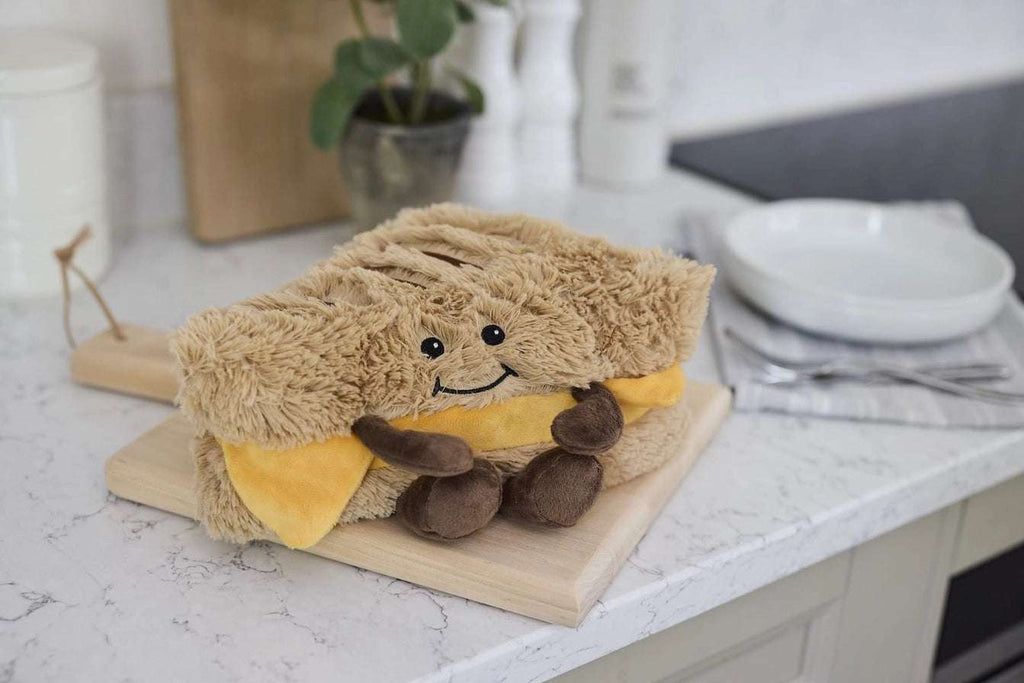 Warmies Grilled Cheese - Plush toy  as a sandwich on a wooden board in a kitchen setting