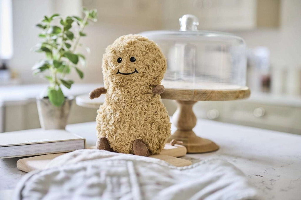 Warmies Peanut - Plush toy peanut with brown feet and arms, sitting in a kitchen